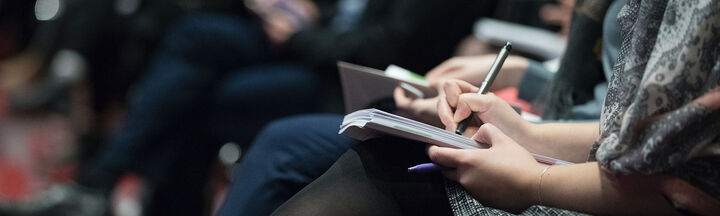 A row of seated conference delegates taking notes