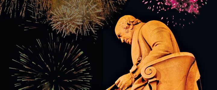 The James Watt statue at the London Campus lit up by fireworks exploding overhead