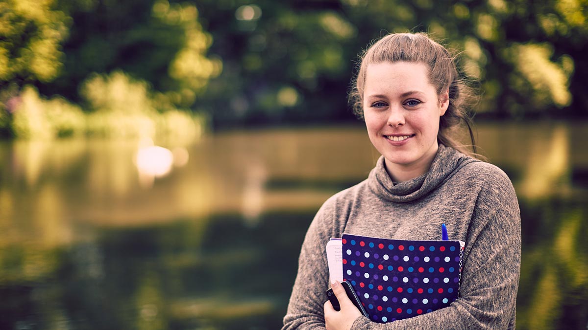 Female student holding a folder beside the loch in summer, London Campus