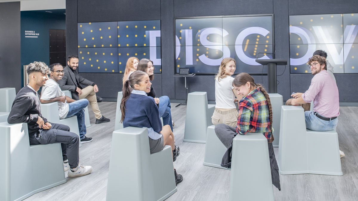 A diverse group of students seated on chairs in front of a massive screen.