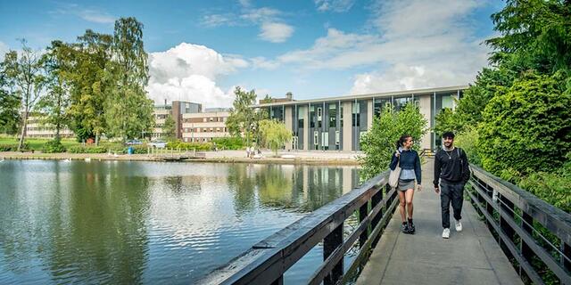 Two students walk across the bridge over the loch, London Campus